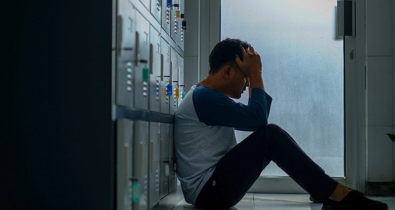teen sitting in school hallway depressed
