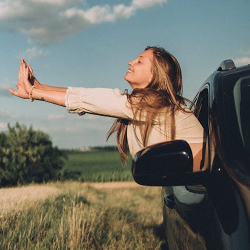 girl hanging out car window riding down the road